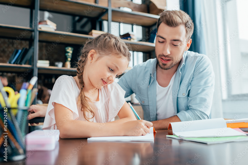 handsome young father doing homework with adorable daughter