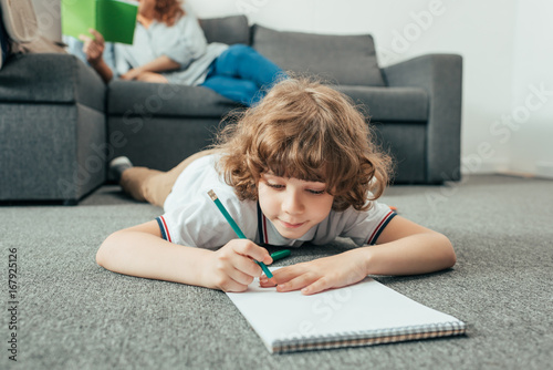 adorable little boy doing homework on floor