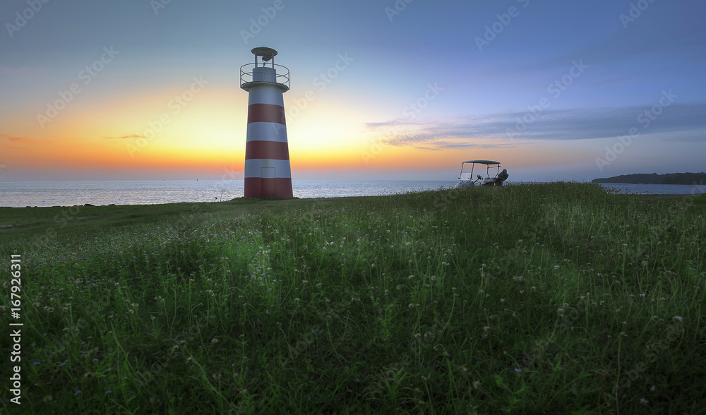 Lighthouse at the field with grass flowers at sunset.