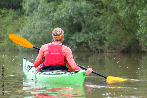 Girl in green kayak kayaking in wild Danube river on biosphere reserve in spring