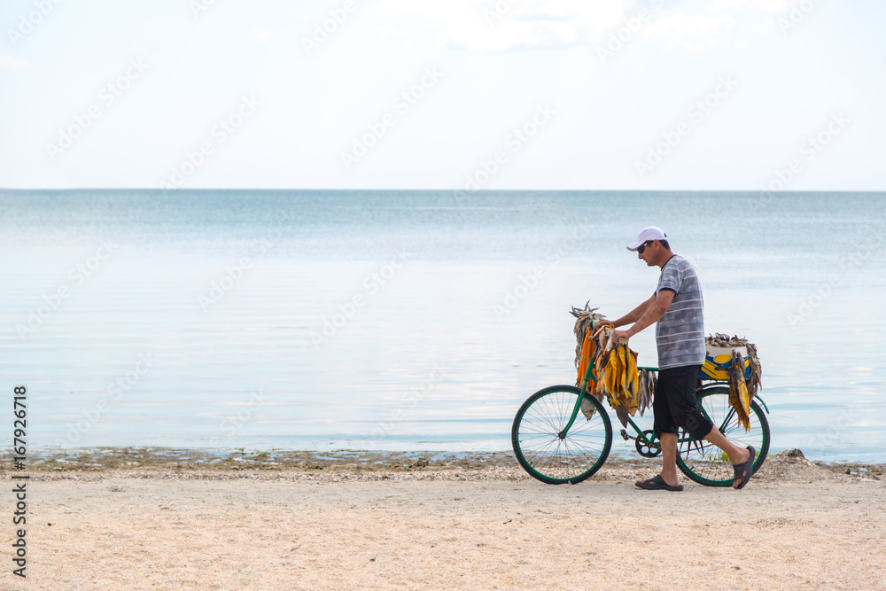 Seller of fish sells fish on the beach by bike