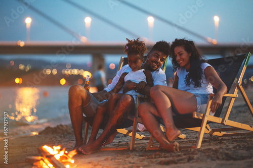 Canvas Print Young mixed race family sitting and relaxing at the beach on a beautiful evening