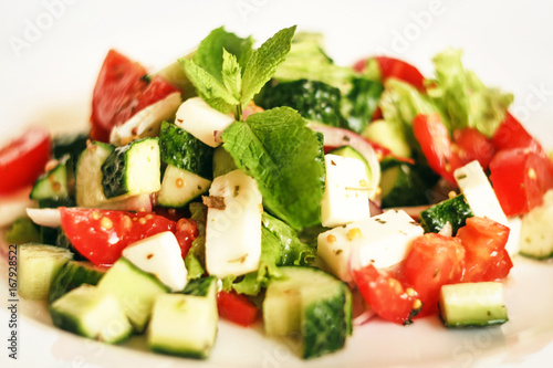 Salad of cucumbers, tomatoes, mozzarella cheese, lettuce, onions, spices and olive oil. Healthy food. Tomato, cucumber, mozzarella cheese, onion, lettuce.