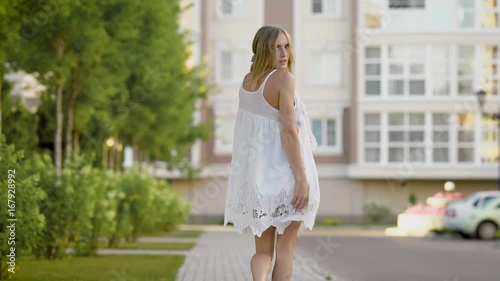 Gorgeous young attractive blonde woman in a white lace dress goes for stroll and gives you alluring look photo