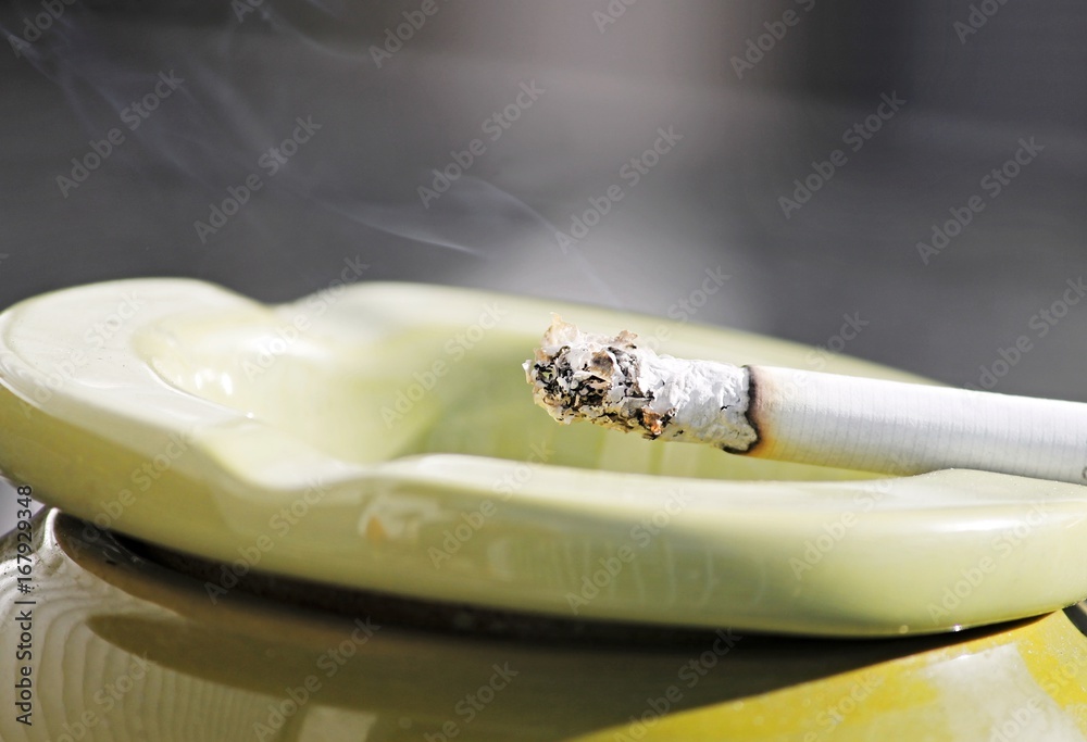 Aschenbecher mit brennender Zigarette auf blauem Hintergrund