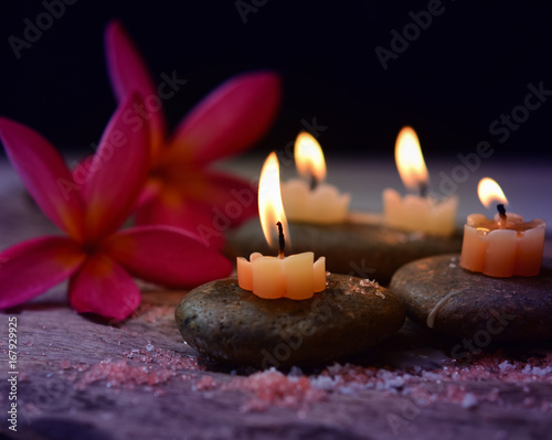 Soft Light and candles scented with refreshing fragrance and salt scrub on black stones, including plumeria flower, spa concept, Thai massage on black background.