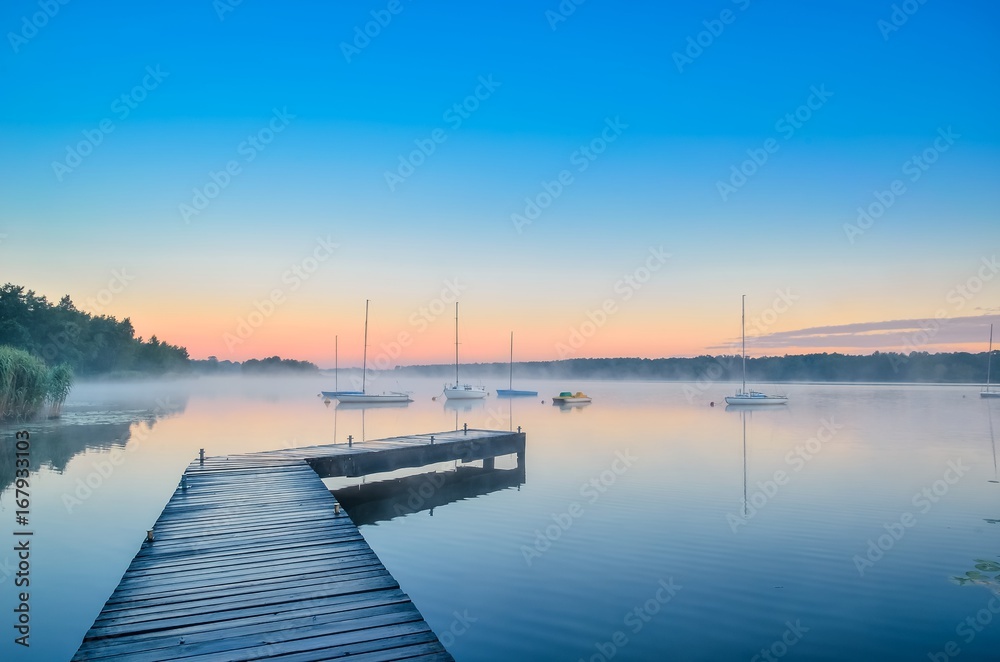 Summer afternoon landscape. Wooden pier and boat on the water at sunrise.