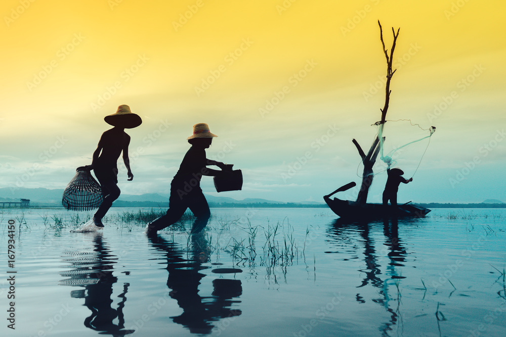 Children boy and girl catching fish, Fisherman fishing nets job lifestyle  on boat at lake, river sunset thailand silhouette. Stock Photo