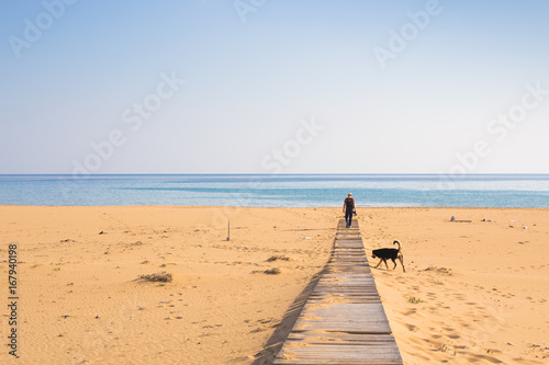 Man with dog walking on the wooden path on the beach and looking into the distance of the ocean © satura_