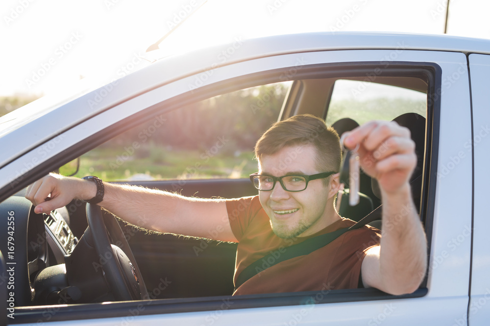 Naklejka premium Young man smiling and holding key in his car. Auto purchase and people concept
