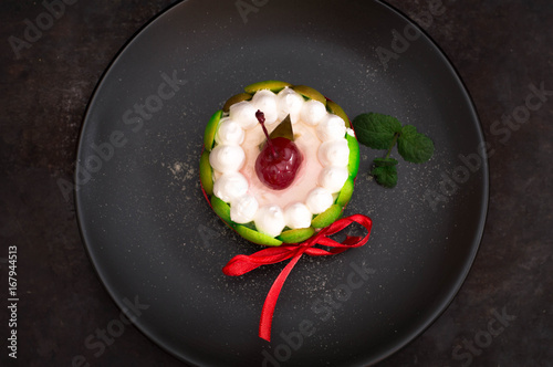 Fruit dessert tart with whipped sweet curd cream and with sweet cherry on top. Old black background. Close-up. Top view photo