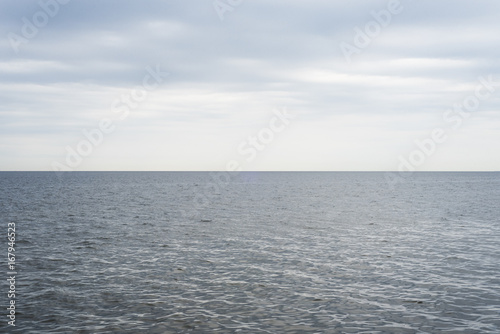 The calm blue-gray ocean waters meet the cool, cloudy blue overcast sky, with a perfectly straight horizon line.
