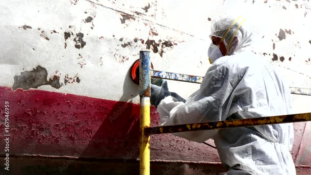 Working people tear off paint on metal in repairs process at shipyard. Workers in overalls reconstruct at ship repair yard outdoors in port. Working people tear off paint on metal in repairs process at shipyard. Workers in overalls reconstruct at ship repair yard outdoors in port.