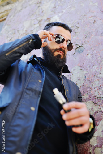 Bearded young man smokes an electronic cigarette or vape