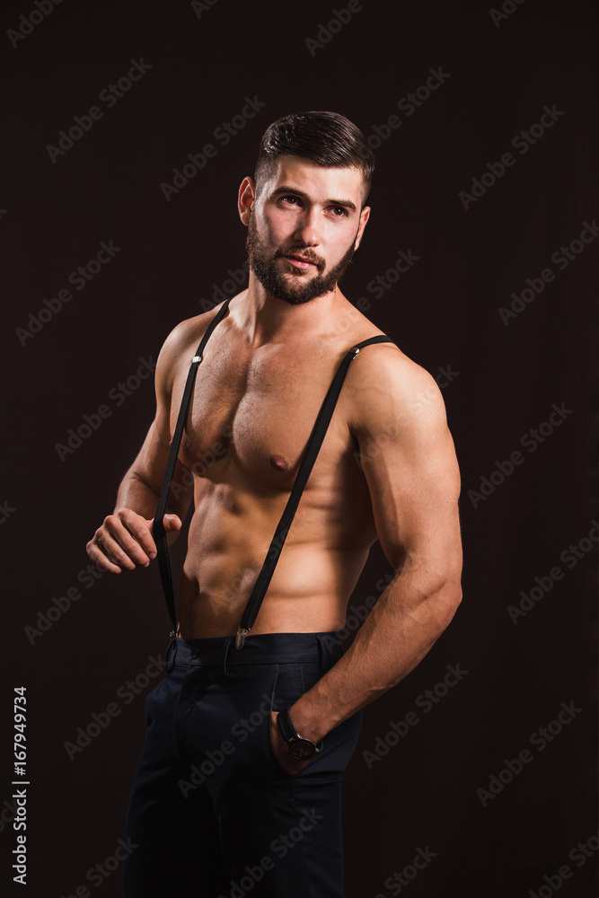 Fototapeta premium Young handsome muscular man with a beard, posing on a black background