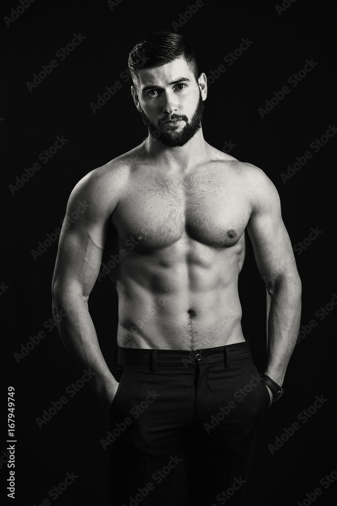 Naklejka premium Young handsome muscular man with a beard, posing on a black background