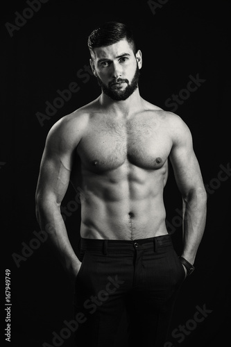 Young handsome muscular man with a beard, posing on a black background