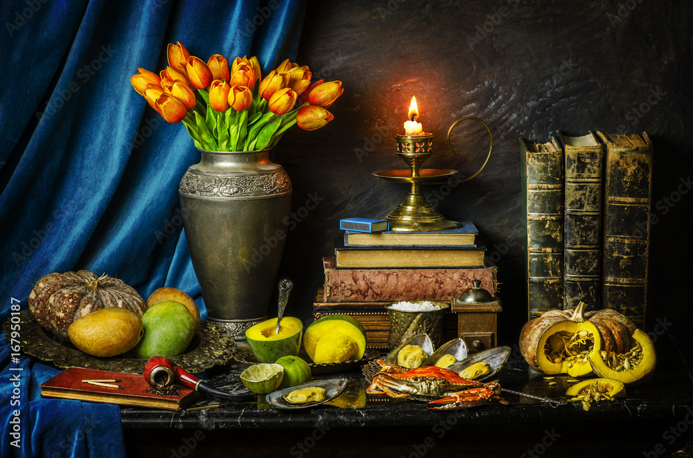 Classic still life with beautiful tulip flowers placed with fresh mangoes,pumpkins,lemon,crab,mussels,illuminated candle,old books and pipe on vintage background