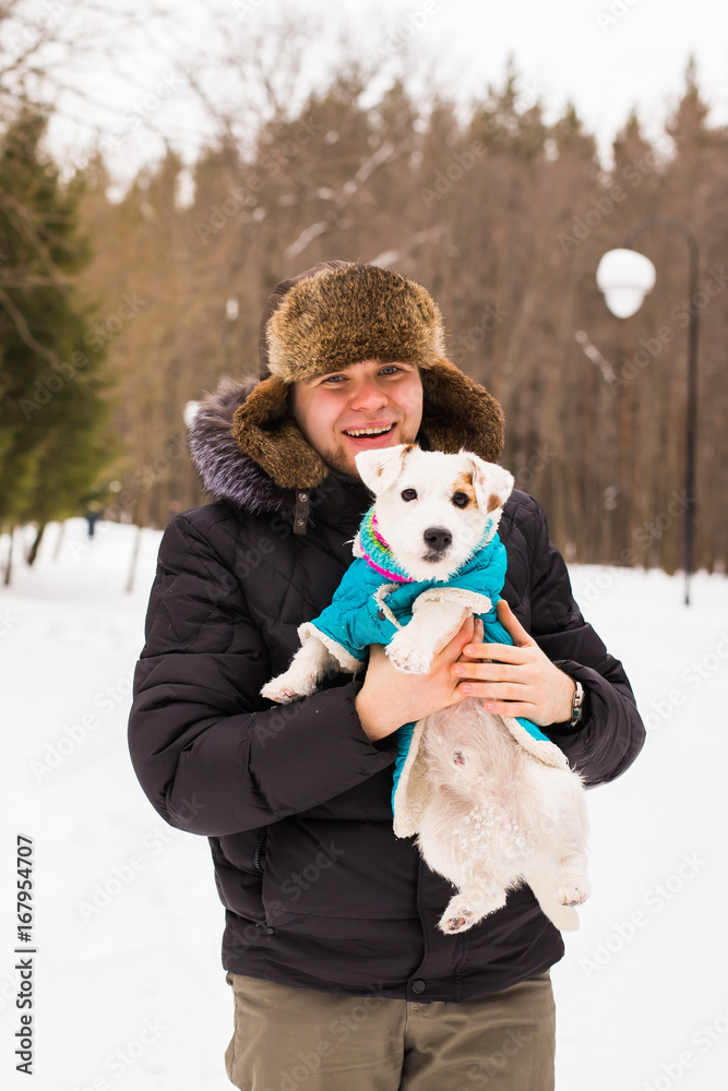Pet owner, dog, and people concept - Young smiling caucasian man holding Jack Russell terrier outdoor in winter time. Pet owner, dog, and people concept - Young smiling caucasian man holding Jack Russell terrier outdoor in winter time.