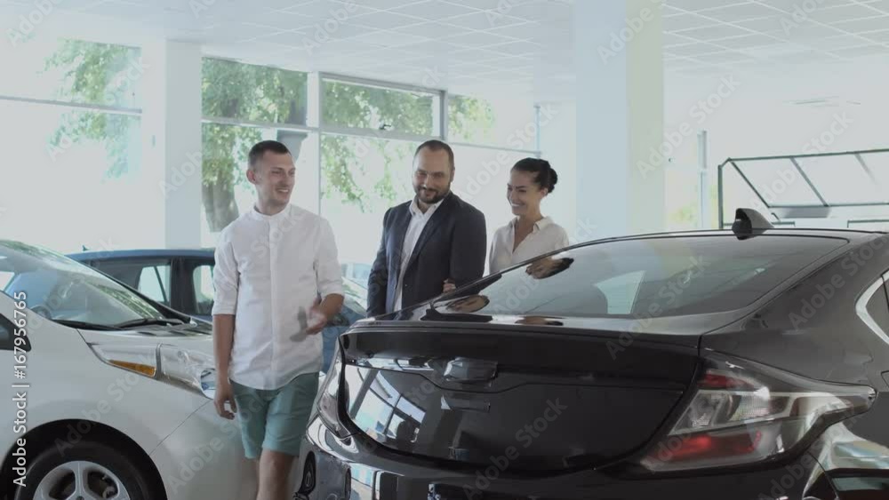 The salesman tells about automobile to a young couple in car dealership The salesman tells about automobile to a young couple in car dealership