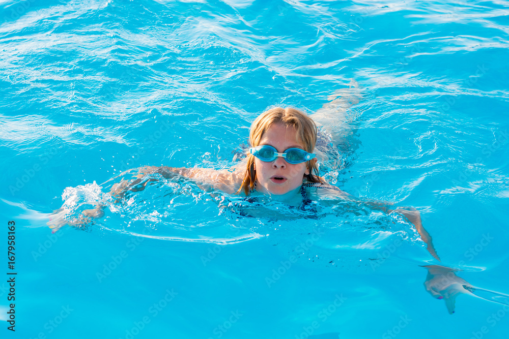 Girl swims in the pool with glasses for swimming
