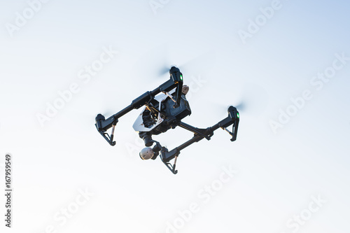 White drone, quadrocopter with photo camera flying in the blue sky.