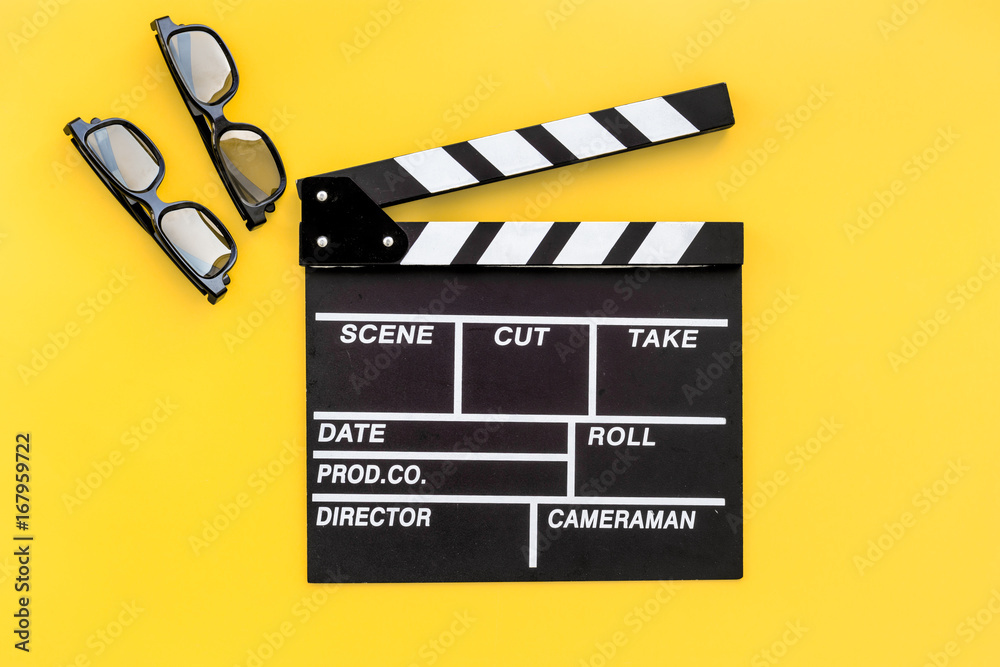 Filmmaker accessories. Clapperboard and glasses on yellow background top view