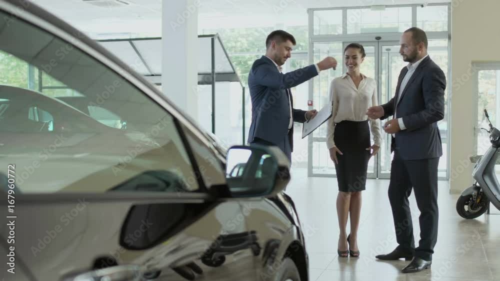 The couple signs the contract of buying car in the car showroom and gets key The couple signs the contract of buying car in the car showroom and gets key