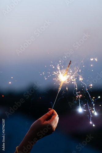 Woman's hand holding sparkler to the sky at twilight