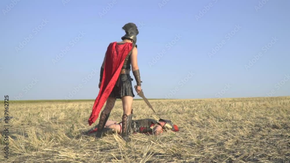 The gladiator in armor turns over the lying enemy and is going to kill him with a sword, slow motion