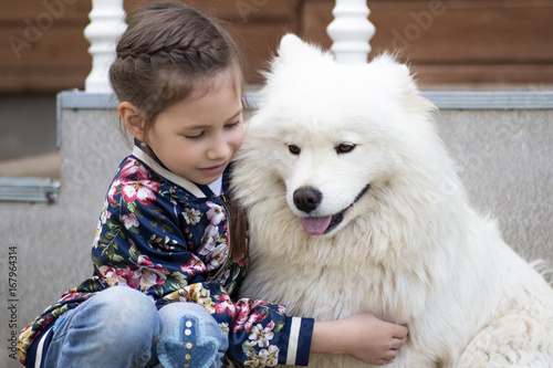 Cute little girl hugging a white dog in park. Good sunny weather,bright sunlight and cute models.
