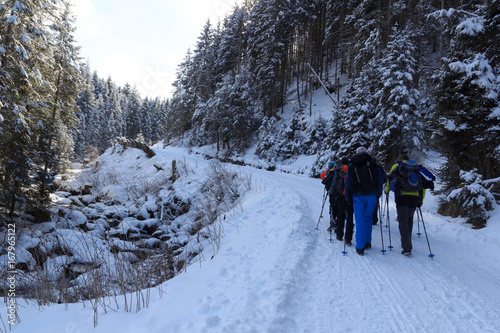 Group of people hiking on wintery snowy path in Stubai Alps mountains and small river, Austria