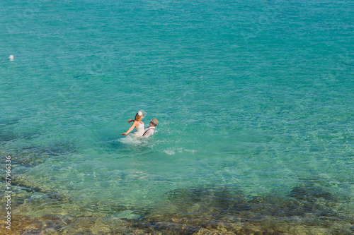 Romantic newly-married couple enjoying a summer vacation. Young groom lifting his bride in sea. © satura_