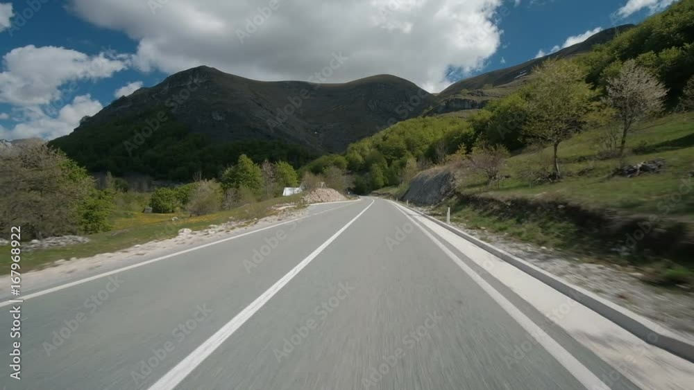 Car moves along suburban roadway in summer day. Vehicle quickly drives over road. Car moves along suburban roadway in summer day. Vehicle quickly drives over road.