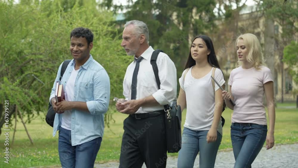 Students and teacher walking in park near college, discussing science project Students and teacher walking in park near college, discussing science project