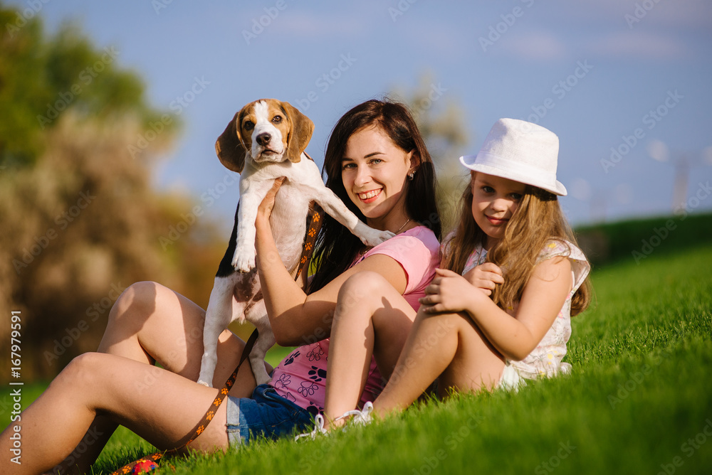 Young woman, her teenage little and their small beagle dog in the park