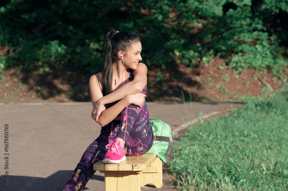 Naklejka premium Concept of sport and lifestyle - young woman having a rest after playing sports smiling sitting on a bench, outdoors