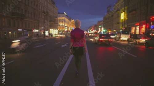 Night dark view of a road and back view of girl going at center of road when cars are moving, Nevsky prospect, Saint Peterburg, Russia photo