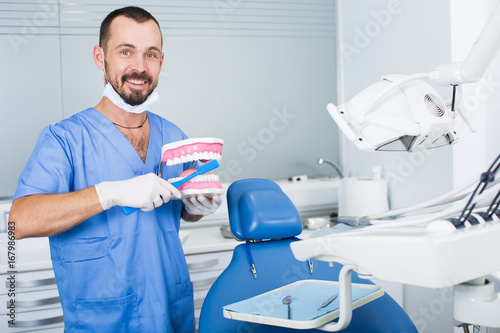 Dentist in uniform with maket of jaw is telling about healthcare