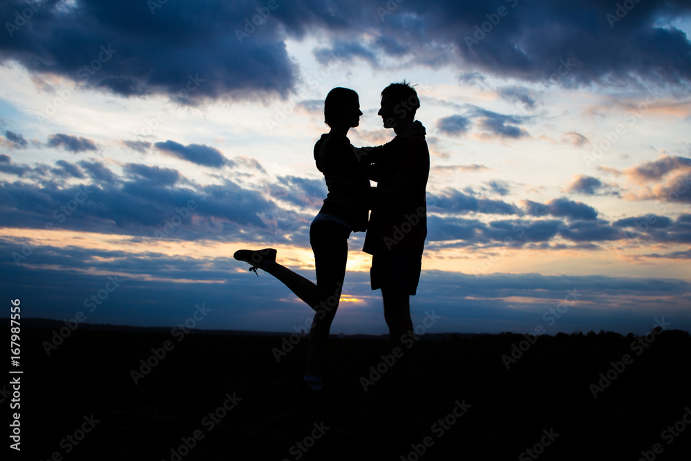 Silhouette lovely couple in a field at sunset with a dramatic sky on a background