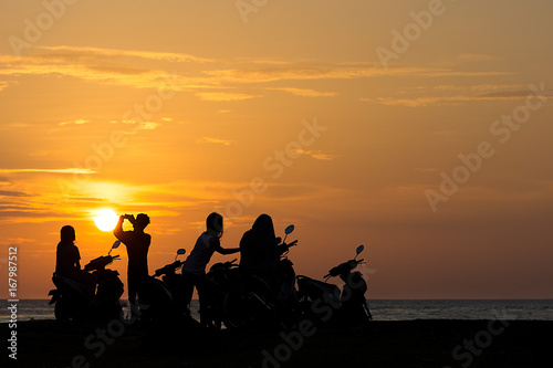 Group Gang of Teenagers Young Adults watch a beach side sun set on their scooters.