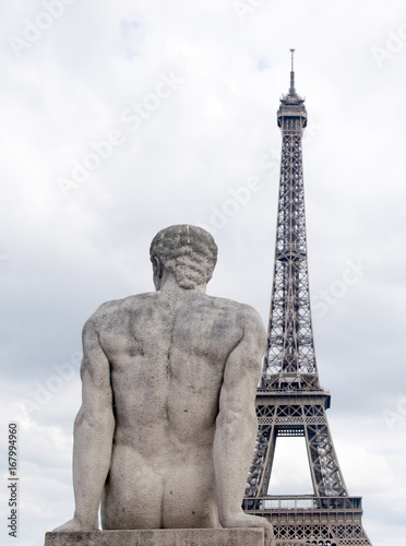Paris France Eiffel Tower close-up with stone statue of seated man from the back looking at dusk sky