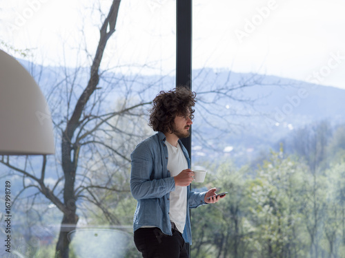 young man drinking coffee and using a mobile phone at home