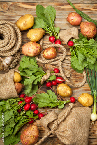 Fresh vegetables potatoes  radishes  onions  rope and bag on a wooden background