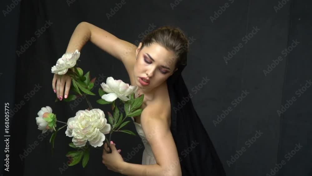 A girl in a white dress with a black cloth thrown over her legs posing with a branch of white flowers