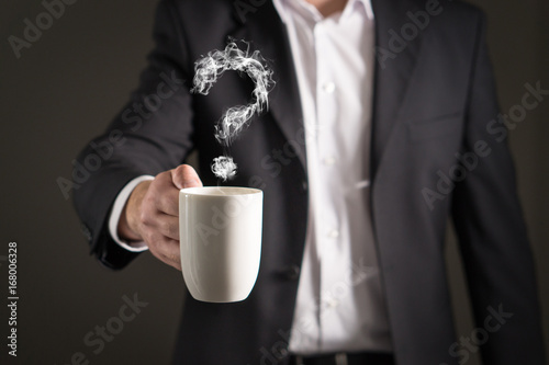 Question mark from coffee steam. Smoke forming a symbol. Business man in a suit holding a hot beverage in a mug and tea cup.