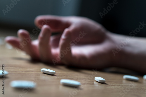 Drug addiction, medical abuse and narcotics hook and dependence concept. Drug addict with withdrawal symptoms lying on floor. Tablet overdose. Suicide and death. Hand surrounded by many pills. photo