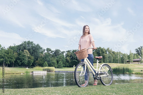 Young woman with vintage bicycle on lawn near the lake
