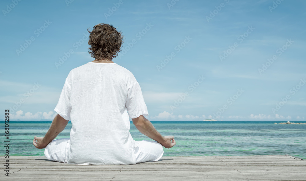 Young man sitting in the lotus position and meditating on the beach close up Young man sitting in the lotus position and meditating on the beach close up