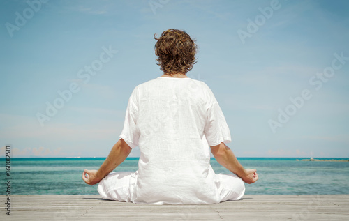 Young man sitting  in the lotus position and meditating on the beach close up